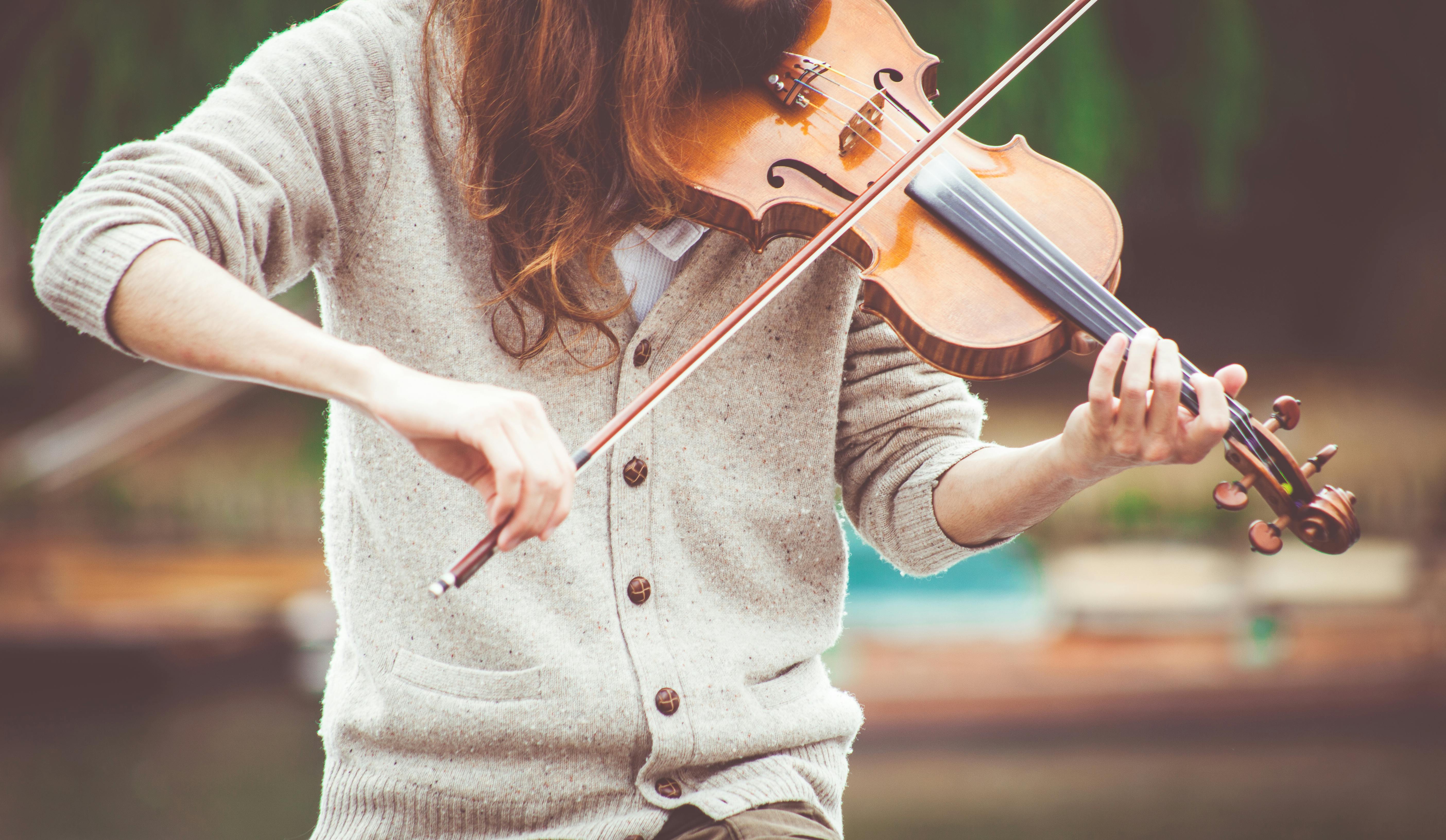 A violinist playing outdoors with a forest behind them