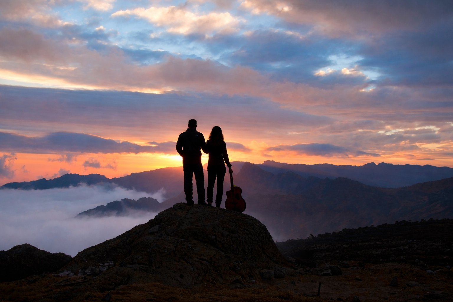 Two Naturals on a mountain summit at golden hour, guitar in hand